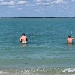 Rear view of men fishing in sea against sky