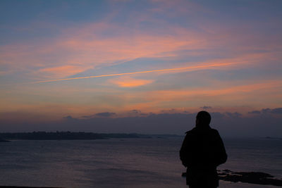 Silhouette man looking at sea against sky during sunset