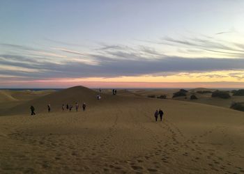 People at beach against sky during sunset