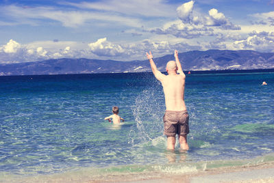 Full length of father and son standing in sea against sky