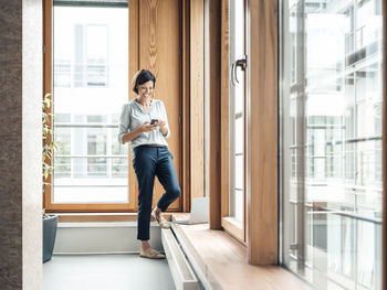 Full length of woman standing by window at home
