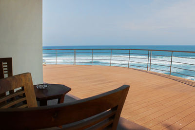 Empty chairs and table by sea against sky