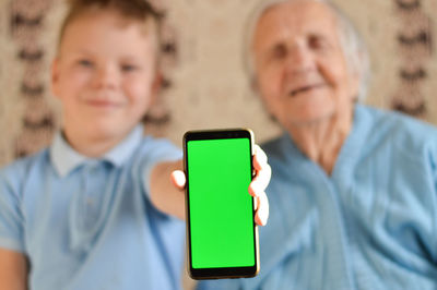  boy and a grandmother who are sitting next to each other and holding green screen of a smartphone.