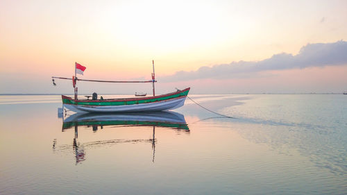 Fishing boat moored in sea against sky during sunset