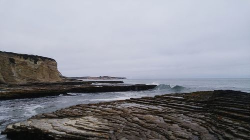 Scenic view of sea and cliff against cloudy sky