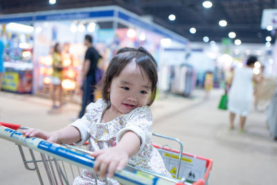 Baby girl sitting in shopping cart at supermarket