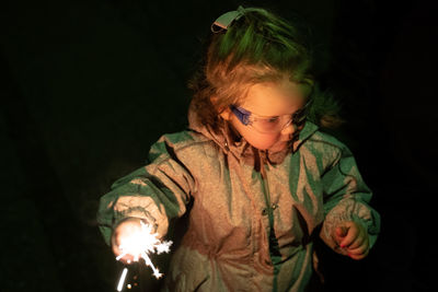 Full length of boy holding illuminated lighting equipment against black background