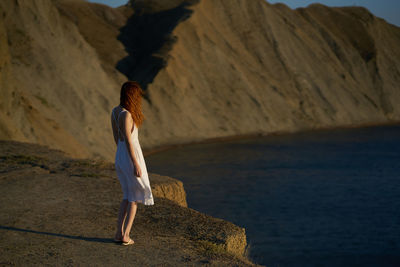 Rear view of woman standing on rock by sea