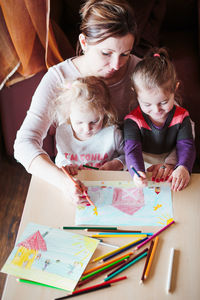 High angle view of mother and daughters painting on paper at home