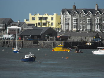 Sailboats moored on sea by buildings in city against sky