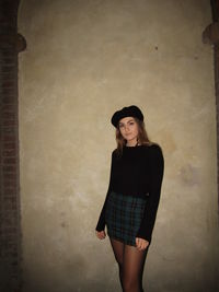 Portrait of young woman standing against wall