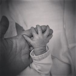 Cropped image of person holding baby hand sleeping on bed at home