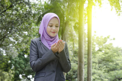Young woman in hijab praying against trees