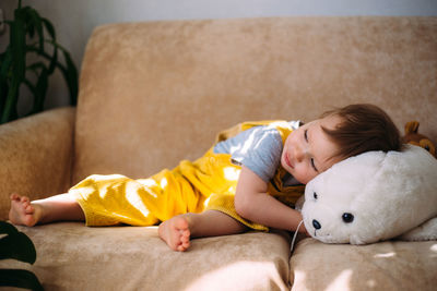 Funny little child is having fun, playing with soft toys on the couch at home.