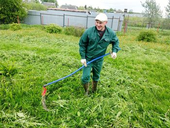 Smiling mature man raking grassy field by lake