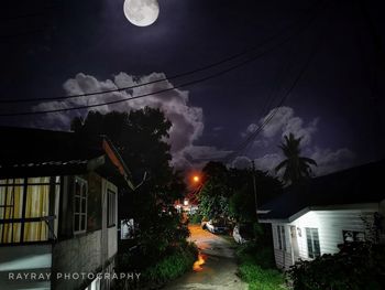 Illuminated street amidst buildings against sky at night