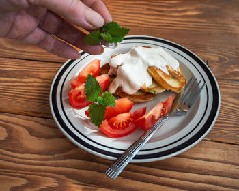 A female hand lays a sprig of mint on a pancake house. pancakes with sour cream on a wooden table