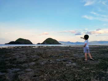 Rear view of boy pointing at sea while standing on land against sky