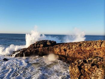 Waves splashing on shore against clear blue sky