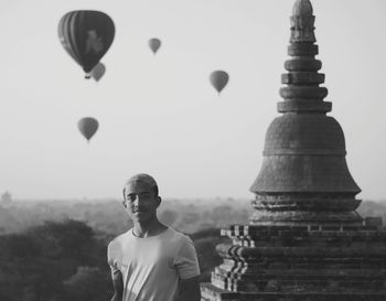 Portrait of man standing at pagoda against hot air balloons