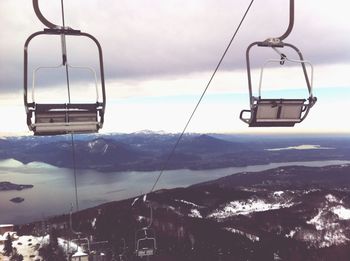 Ski lift over mountains against cloudy sky during winter