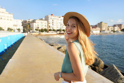 Cheerful stylish woman turns around and smiling at camera on crotone promenade, calabria, italy