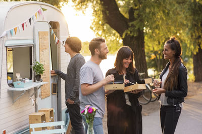 Happy friends having salad while standing on street outside food truck