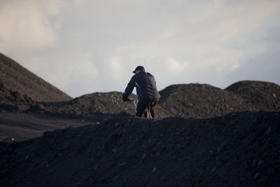 Rear view of man cycling amidst dirt heap