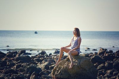 Woman sitting on rock at beach against clear sky