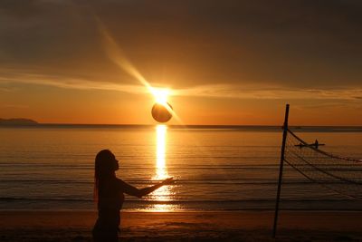 Silhouette woman playing volleyball at beach against sky during sunset