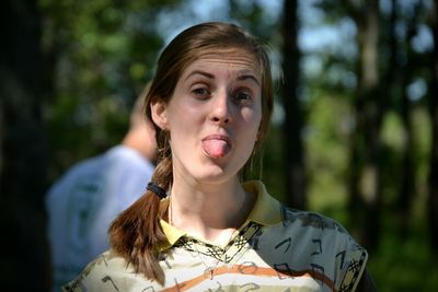 Close-up portrait of young woman sticking out tongue while standing in forest