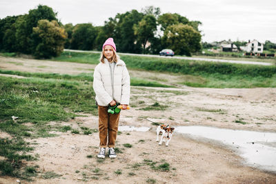 Cute teenage girl walking her dog jack russell terrier on a leash in a field against a background