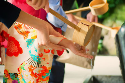 Cropped image of people with ladle at drinking fountain in temple