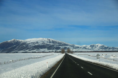 Road leading towards snowcapped mountains against sky