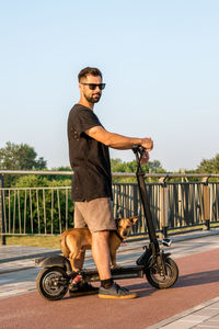 Handsome european man is riding on electric scooter with his small dog.