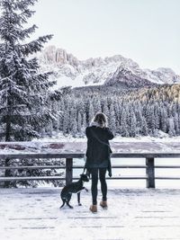 Woman with dog standing on snowy bridge against sky