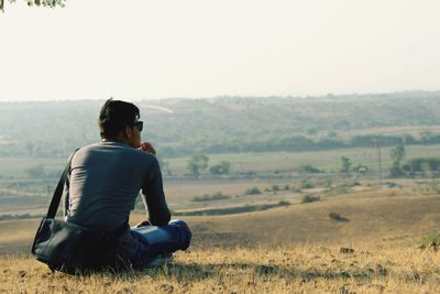 Rear view of man sitting on landscape against sky