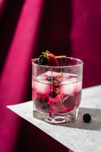 Glass of refreshing cocktail with blackberry and raspberry on wooden toothpick on table