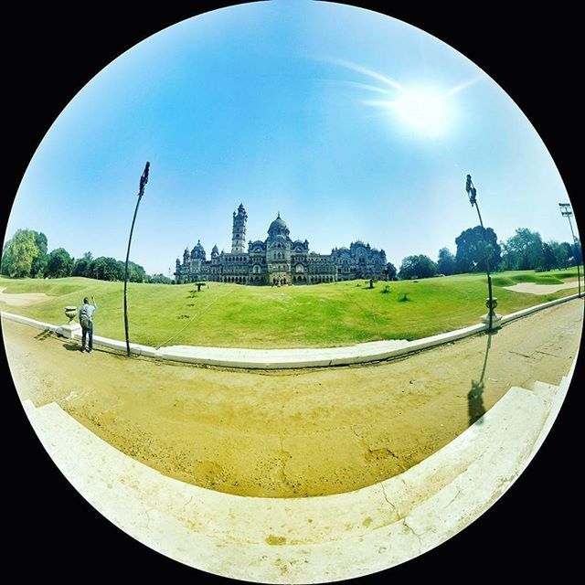 grass, built structure, architecture, sky, building exterior, lawn, sunlight, green color, incidental people, travel destinations, monument, famous place, day, cloud - sky, tree, blue, cloud, history, park - man made space, tower