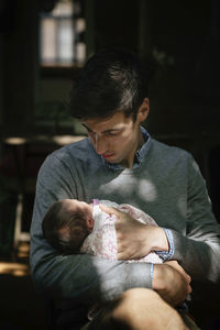 Father carrying newborn daughter while sitting at home