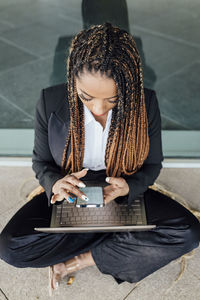 Young businesswoman sitting cross-legged with laptop using smart phone