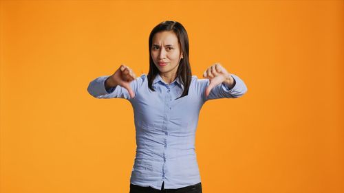 Portrait of young woman standing against yellow background