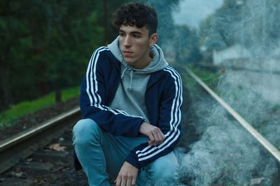 Thoughtful teenage boy crouching on railroad track