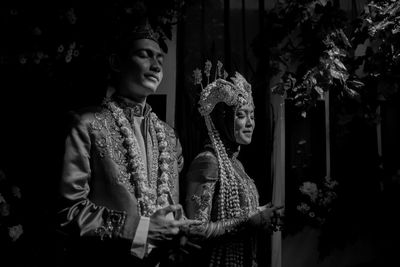 Couples looking away while standing against plants