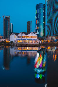 Illuminated buildings by river against sky at night