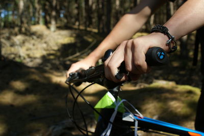 Cropped hands of person holding bicycle handlebar in forest