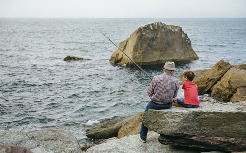 Grandfather and grandson fishing together at the sea sitting on rock