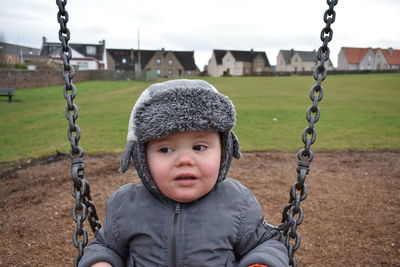 Close-up of cute boy wearing fur hat playing on swing in playground