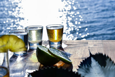 Close-up of tequila shots with lemon on table by sea