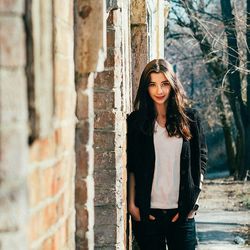 Portrait of beautiful young woman standing against brick wall